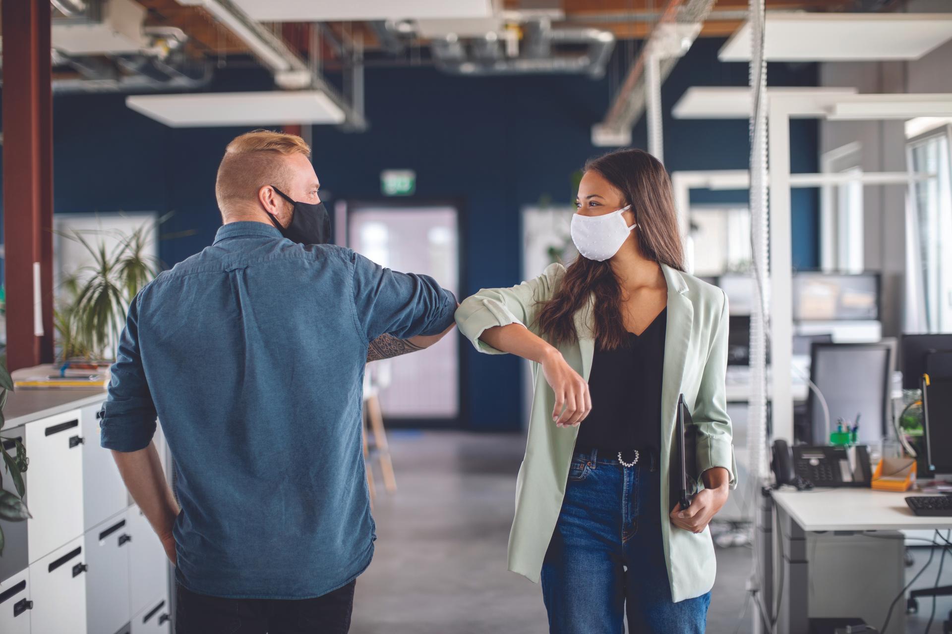 two people wearing masks passing each other in the office
