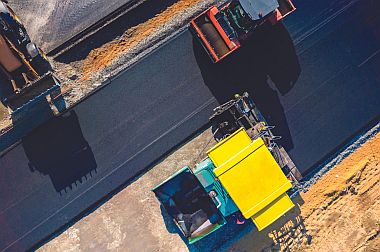 an aerial view of heavy machinery trucks laying asphalt