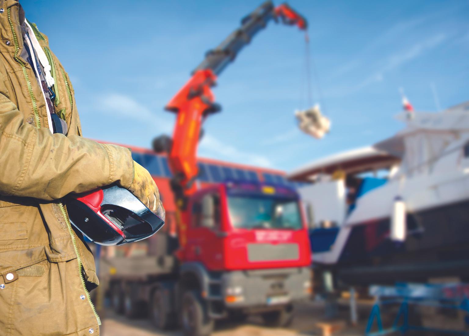 Construction site worker holding a work helmet, with a crane lifting objects in the background
