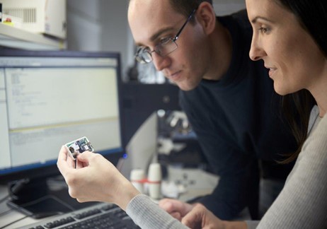 Man with glasses and woman looking at a module in front of a monitor