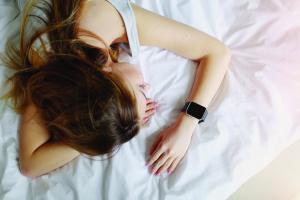bird's eye view of woman sleeping while wearing a sleep-tracker device on her left wrist