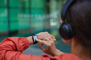 Person using a smartwatch with headphones, representing low-power wearable GNSS positioning applications