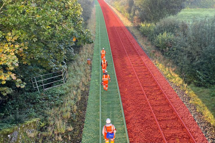A bird's eye view of railway construction workers wearing high-visibility jackets walking next to an open rail track
