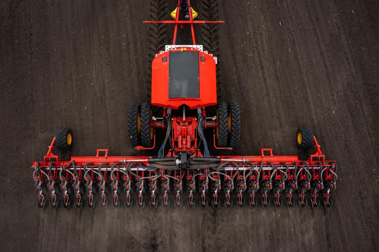 Aerial view of a red agricultural tractor towing a wide precision planter across a plowed field, demonstrating advanced farming machinery used in smart agriculture. Aerial view of a red agricultural tractor towing a wide precision planter across a plowed field, demonstrating advanced farming machinery used in smart agriculture.