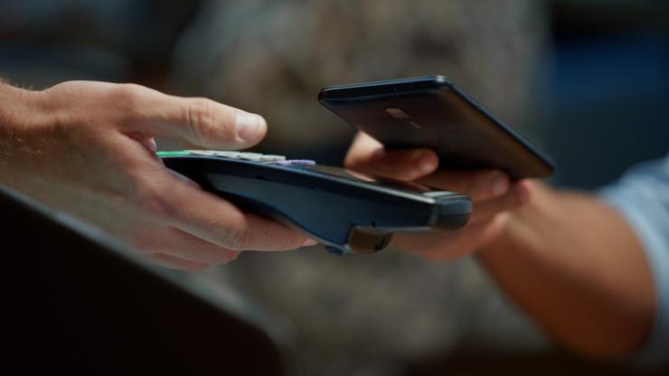 Customer making a contactless payment using a smartphone and wireless POS terminal at checkout.