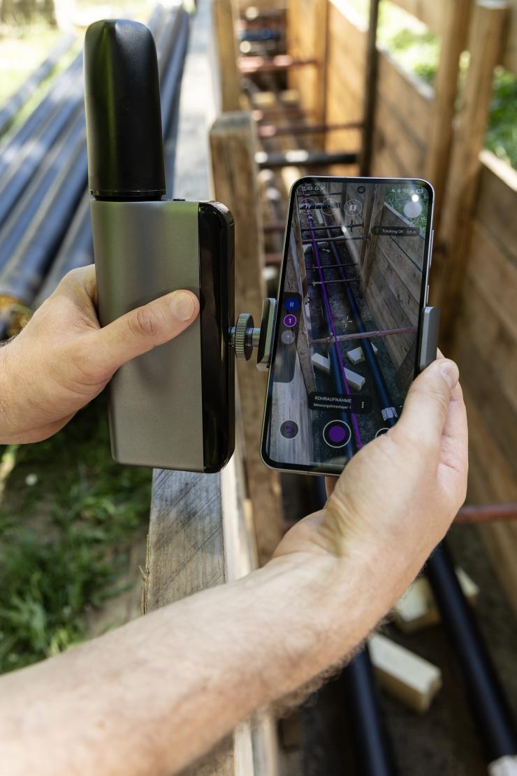 A handheld GNSS receiver paired with a smartphone displaying an augmented reality view of underground utilities for high-precision positioning and utility mapping in the field.