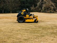 a yellow and black mower sitting on top of a dry grass field