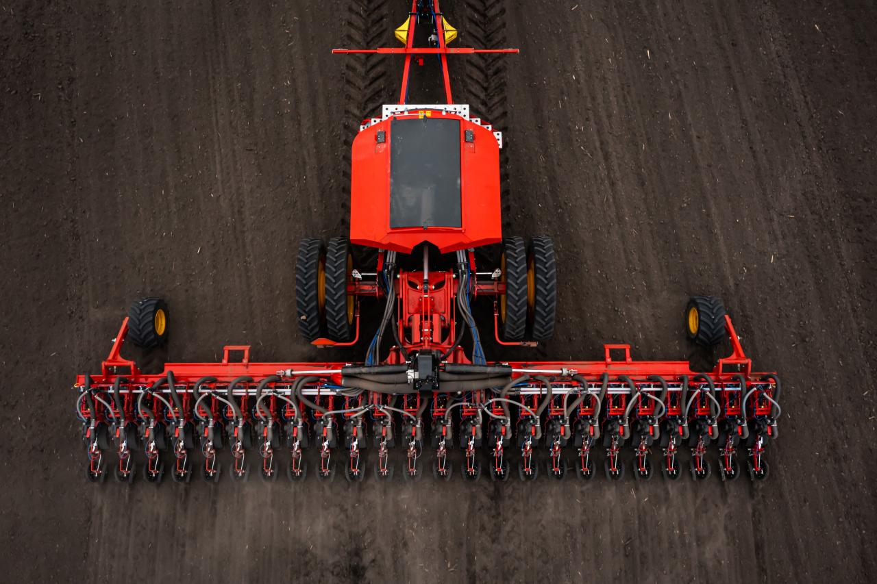 Aerial view of a red agricultural tractor towing a wide precision planter across a plowed field, demonstrating advanced farming machinery used in smart agriculture.