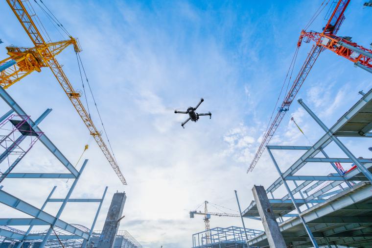 Drone flying above a construction site with cranes and steel structures, demonstrating GNSS supported drone navigation in industrial operations.